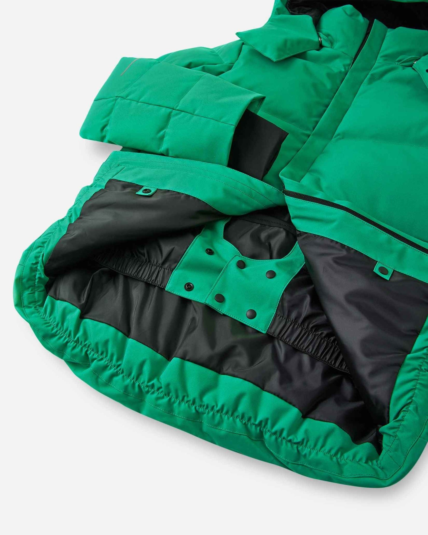 Interior view of the lower half of the green Reima Ranua kids' down ski jacket, featuring a smooth black lining, an adjustable elastic hem, and a built-in snow skirt with snap fasteners to completely block out snow and cold drafts.