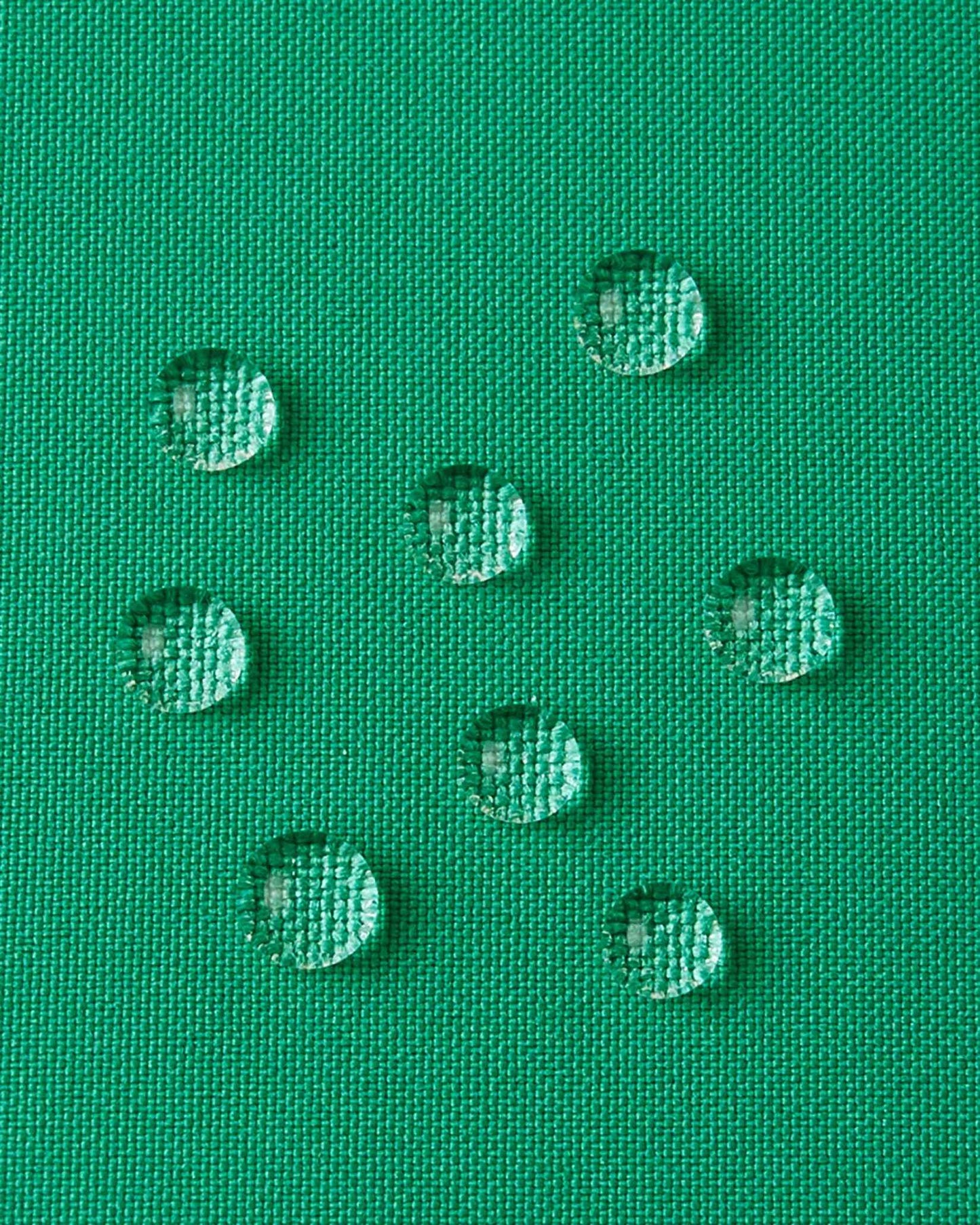A detailed close-up texture shot of water droplets beading up cleanly on the green water-repellent fabric of a Reima Ranua kids' down ski jacket, demonstrating its durable weather-resistant performance for outdoor winter play.
