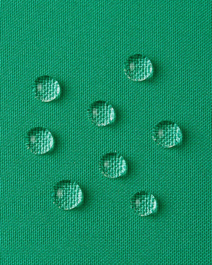 A detailed close-up texture shot of water droplets beading up cleanly on the green water-repellent fabric of a Reima Ranua kids' down ski jacket, demonstrating its durable weather-resistant performance for outdoor winter play.