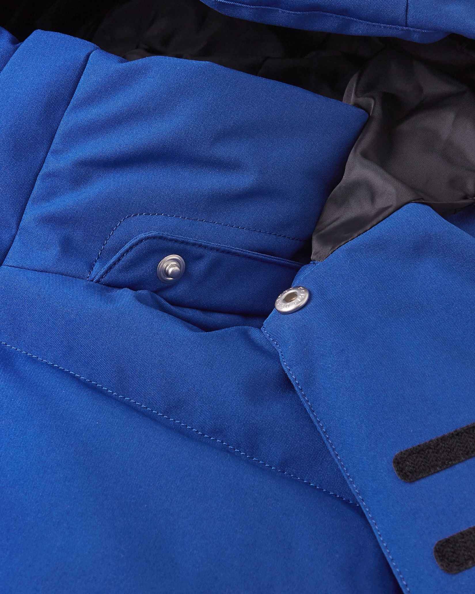 Close-up of the collar area on the Reima Ranua kids' down ski jacket in twilight blue, detailing the secure snap buttons used to attach the safe, easily removable winter hood.