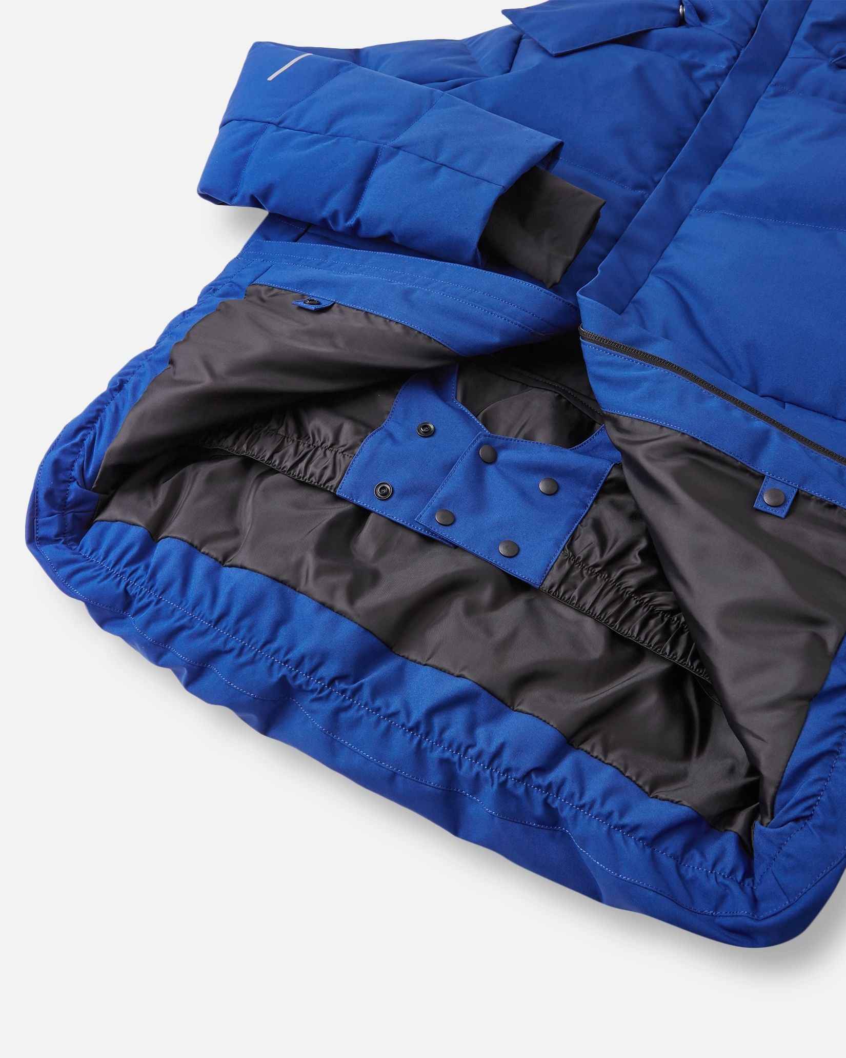 Interior view of the lower half of the twilight blue Reima Ranua kids' down ski jacket, featuring a smooth black lining, an adjustable elastic hem, and a built-in snow skirt with snap fasteners to completely block out snow and cold drafts.
