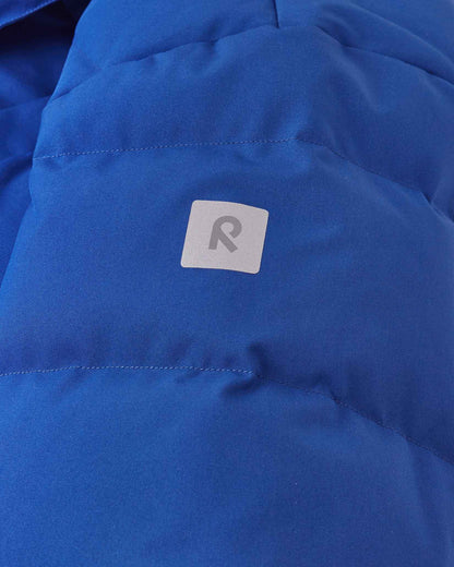 Close-up detail of the twilight blue Reima Ranua kids' down ski jacket, highlighting the horizontal down insulation quilting and a square reflective Reima logo patch designed to enhance winter safety and visibility.