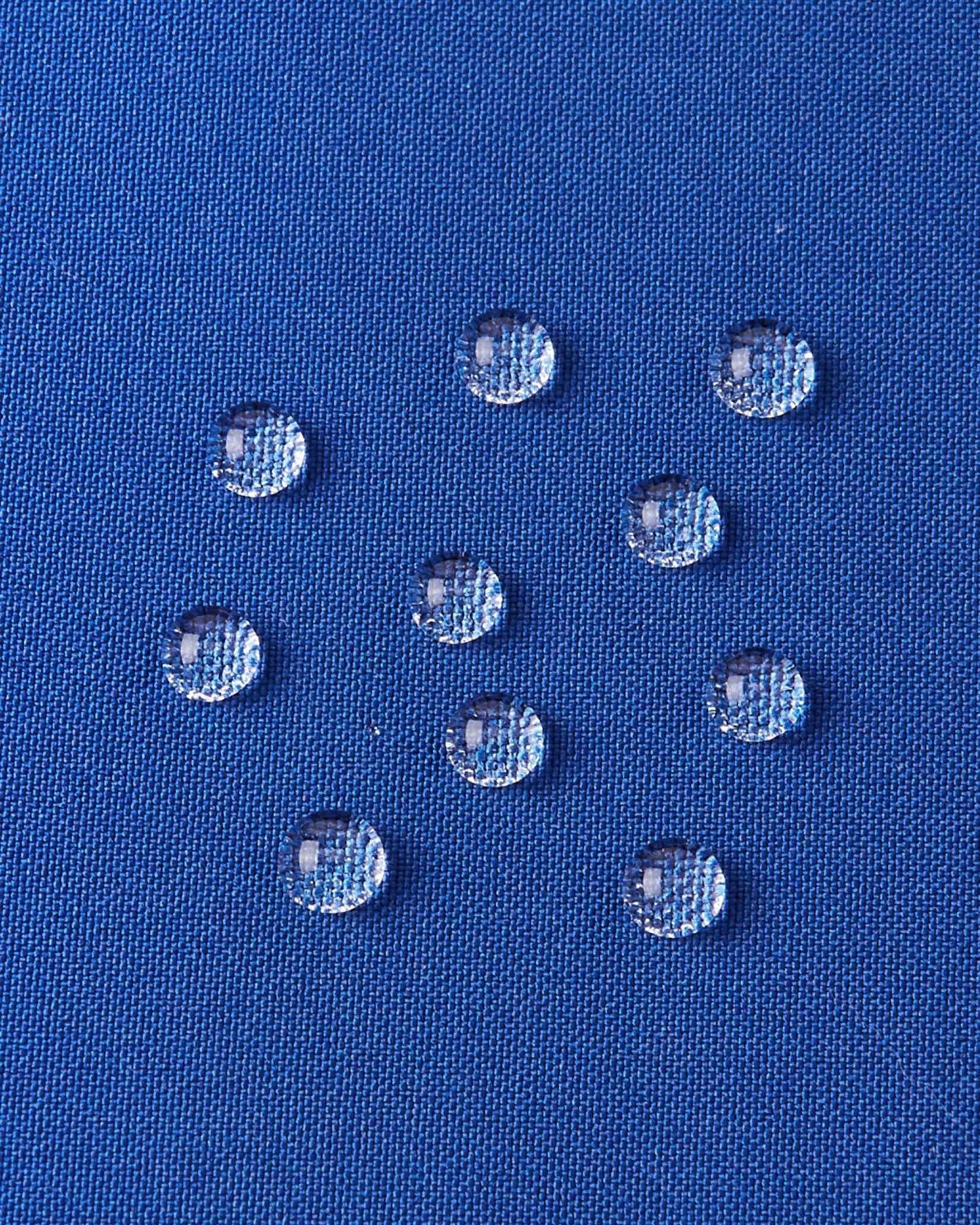 A detailed close-up texture shot of water droplets beading up cleanly on the twilight blue water-repellent fabric of a Reima Ranua kids' down ski jacket, demonstrating its durable weather-resistant performance for outdoor winter play.