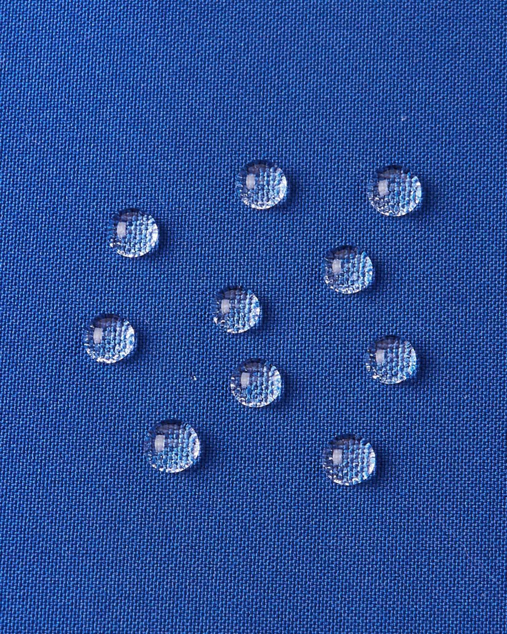A detailed close-up texture shot of water droplets beading up cleanly on the twilight blue water-repellent fabric of a Reima Ranua kids' down ski jacket, demonstrating its durable weather-resistant performance for outdoor winter play.