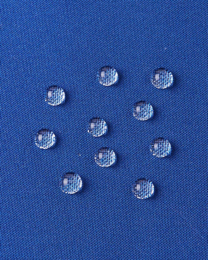 A detailed close-up texture shot of water droplets beading up cleanly on the twilight blue water-repellent fabric of a Reima Ranua kids' down ski jacket, demonstrating its durable weather-resistant performance for outdoor winter play.