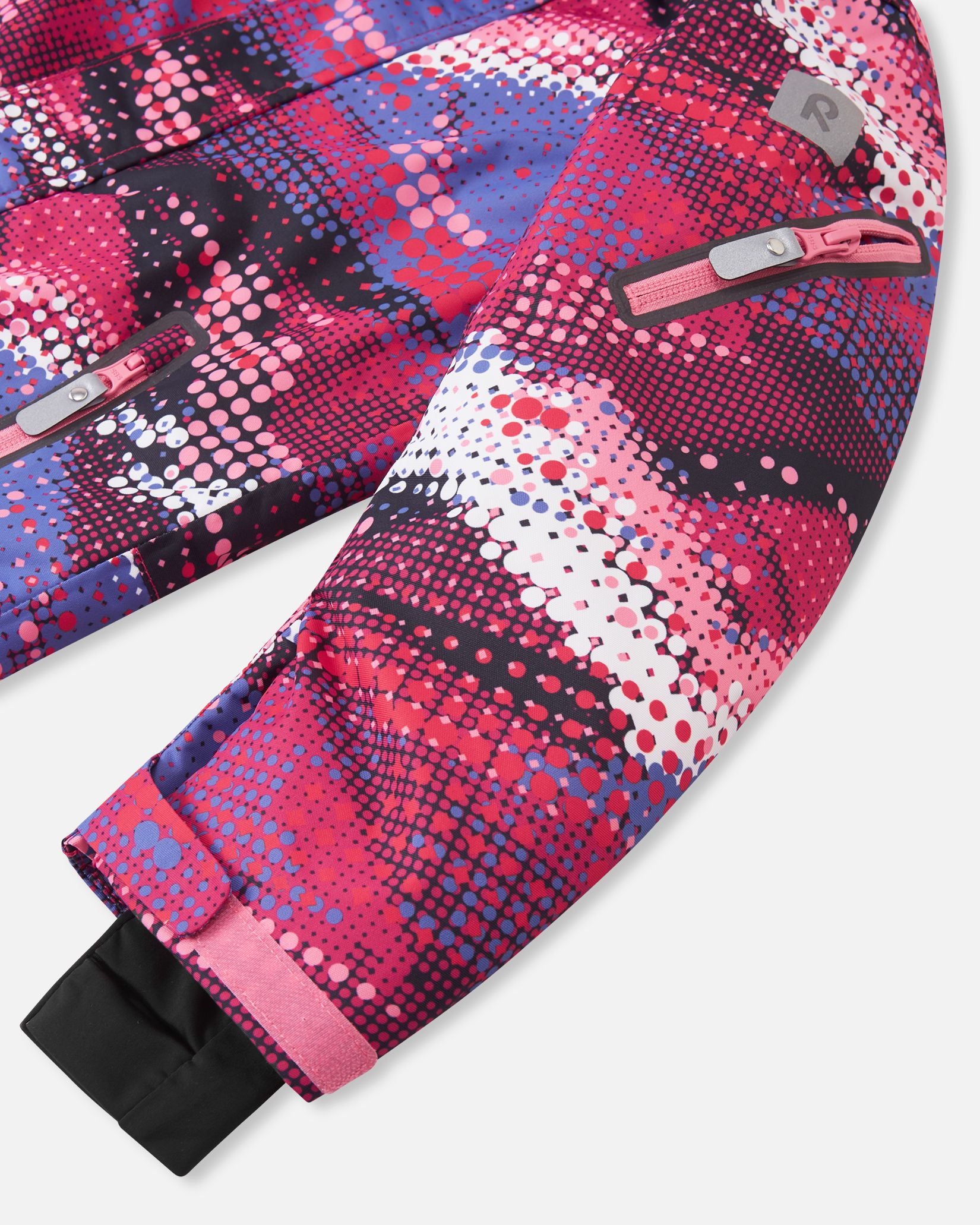 Detail shot of the sleeve on the rosy berry Reima Reach girls' ski suit, featuring a secure zippered ski pass pocket on the forearm, a high-visibility reflective Reima safety patch, and snug inner lycra cuffs to completely lock out snow.
