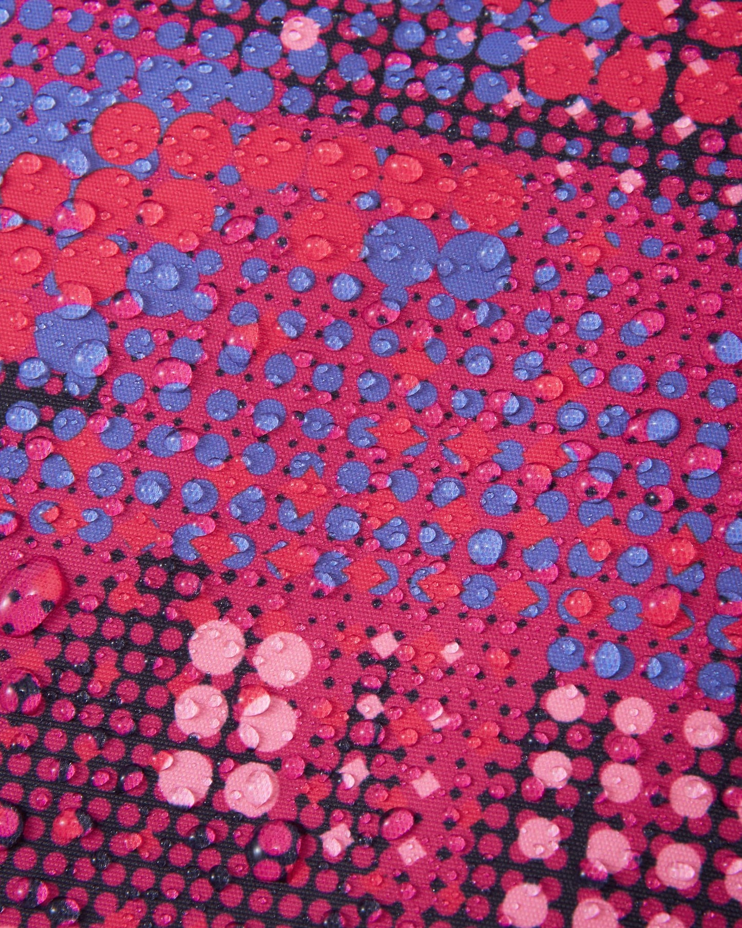 Macro close-up of water droplets tightly beading on the rosy berry patterned Reimatec fabric of the Reima Reach girls' ski suit, demonstrating its extreme high-performance waterproof and weather-resistant surface capabilities.