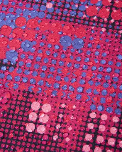 Macro close-up of water droplets tightly beading on the rosy berry patterned Reimatec fabric of the Reima Reach girls' ski suit, demonstrating its extreme high-performance waterproof and weather-resistant surface capabilities.