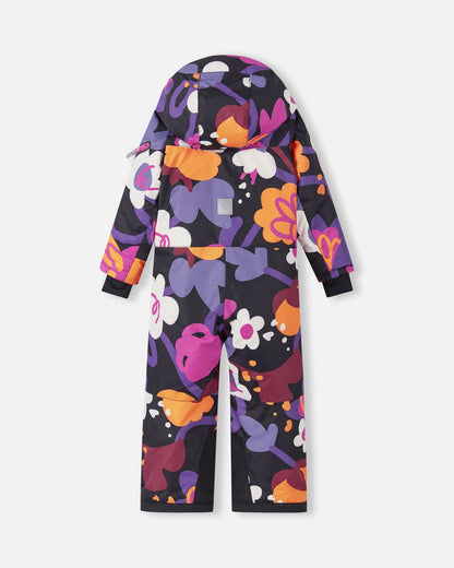 Back view of the Reima Reach kids' ski suit showcasing the bold floral print on a black background, with an attached hood, a reflective safety patch positioned on the center back, and highly durable reinforced black fabric at the inner ankles.