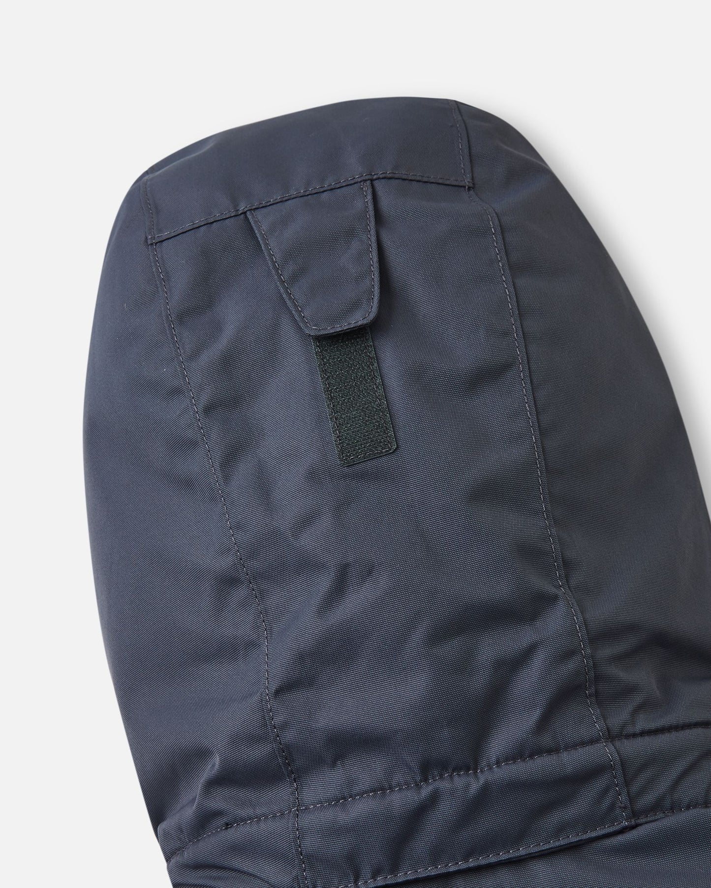 Detail shot of the back of the hood on the soft black Reima Reach kids' ski suit, highlighting the adjustable velcro tab that allows parents to easily customize the hood depth for a secure fit over a ski helmet or winter beanie.