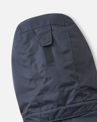 Detail shot of the back of the hood on the soft black Reima Reach kids' ski suit, highlighting the adjustable velcro tab that allows parents to easily customize the hood depth for a secure fit over a ski helmet or winter beanie.