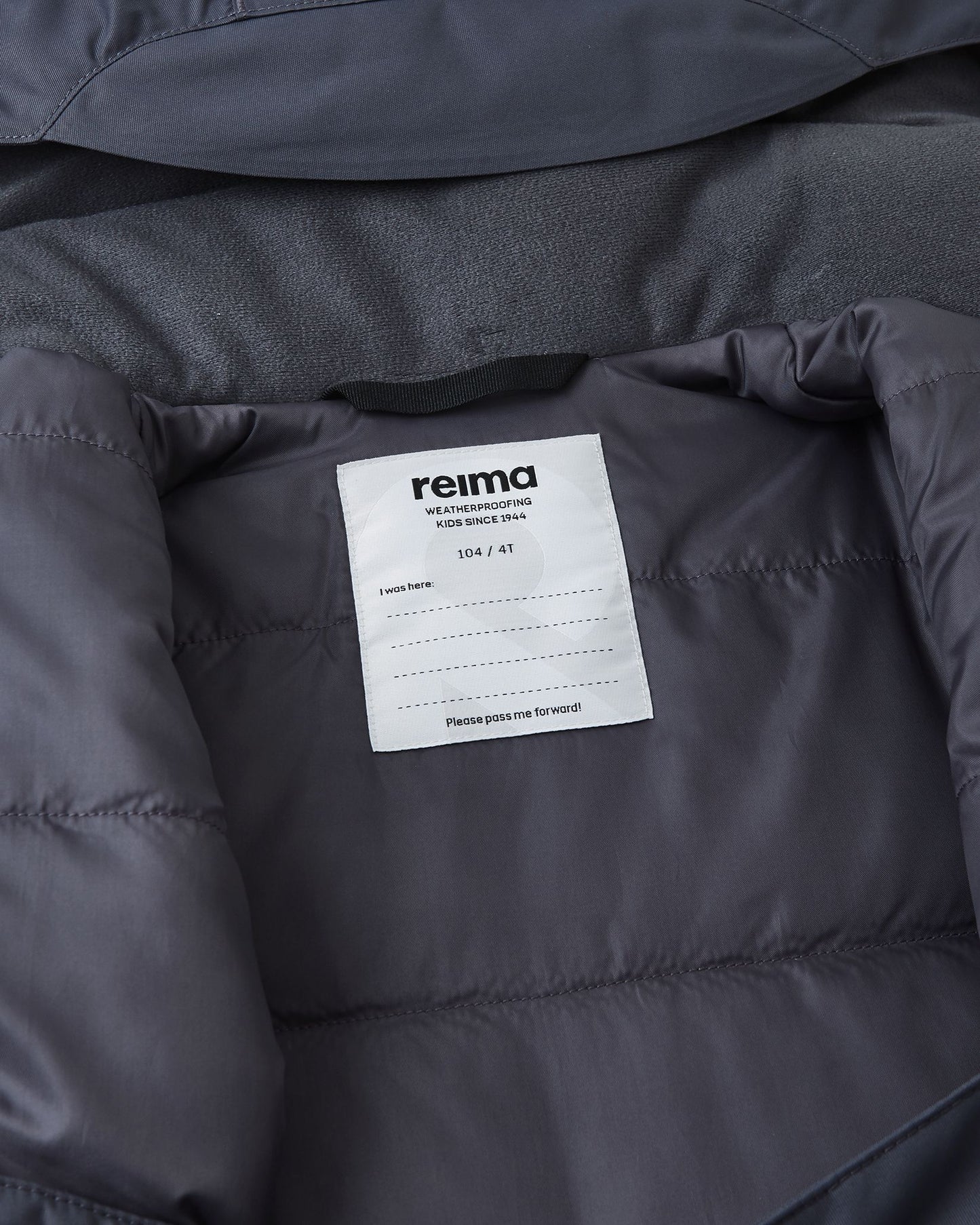 Inside collar view of the soft black Reima Reach ski suit, displaying the cozy fleece lining to prevent chin chafing and a dedicated Reima name tag with multiple lines to encourage sustainable hand-me-downs.
