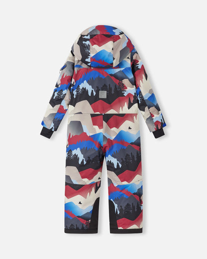 Back view of the Reima Reach kids' winter ski suit in a bold red, blue, and black mountain pattern, showcasing the attached hood, a reflective Reima safety patch on the center back, and durable black reinforced fabric at the inner ankles to resist ski edge wear.