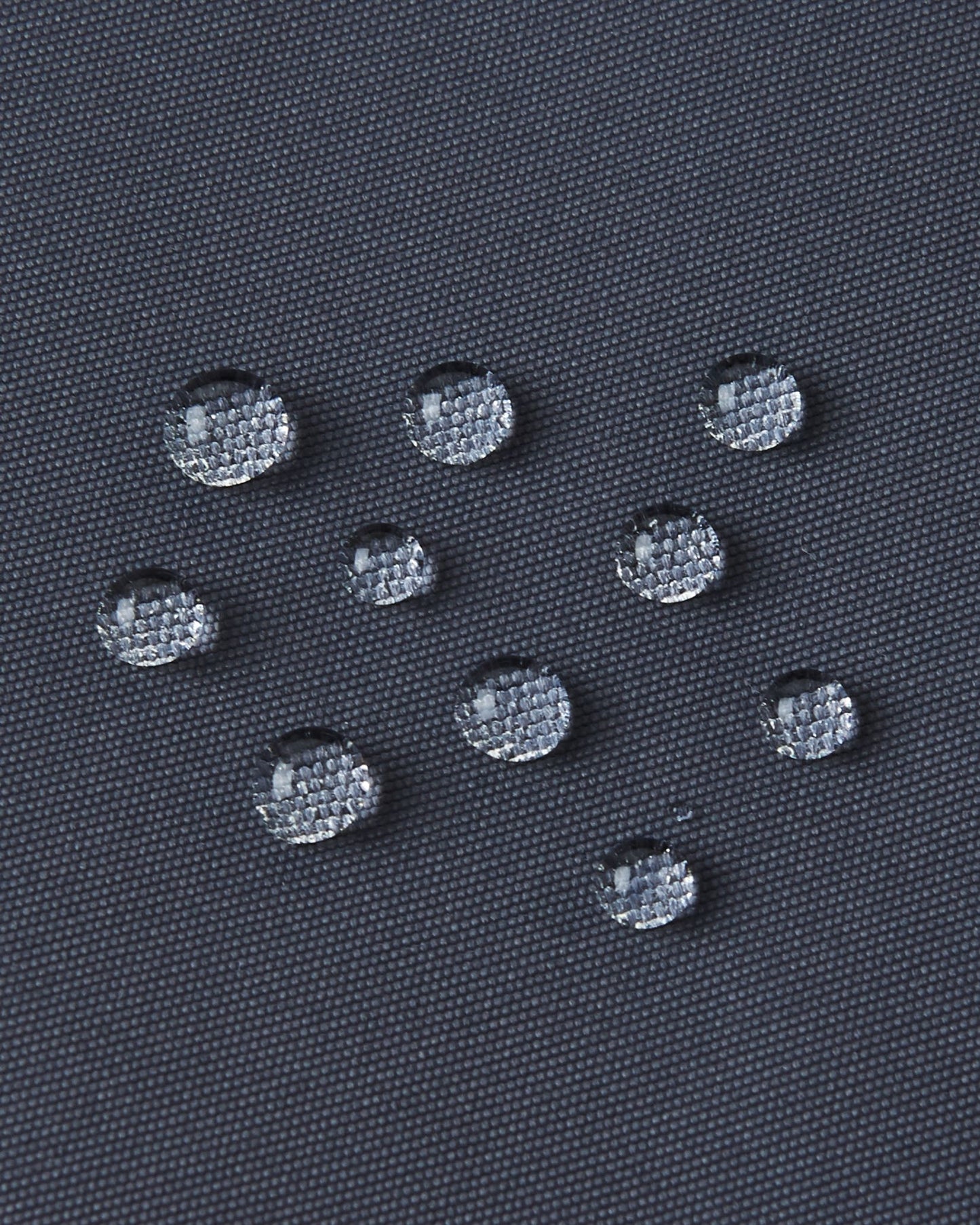 Macro close-up of water droplets tightly beading on the soft black Reimatec fabric of the Reima Reach kids' ski suit, demonstrating its extreme high-performance waterproof and weather-resistant surface capabilities.