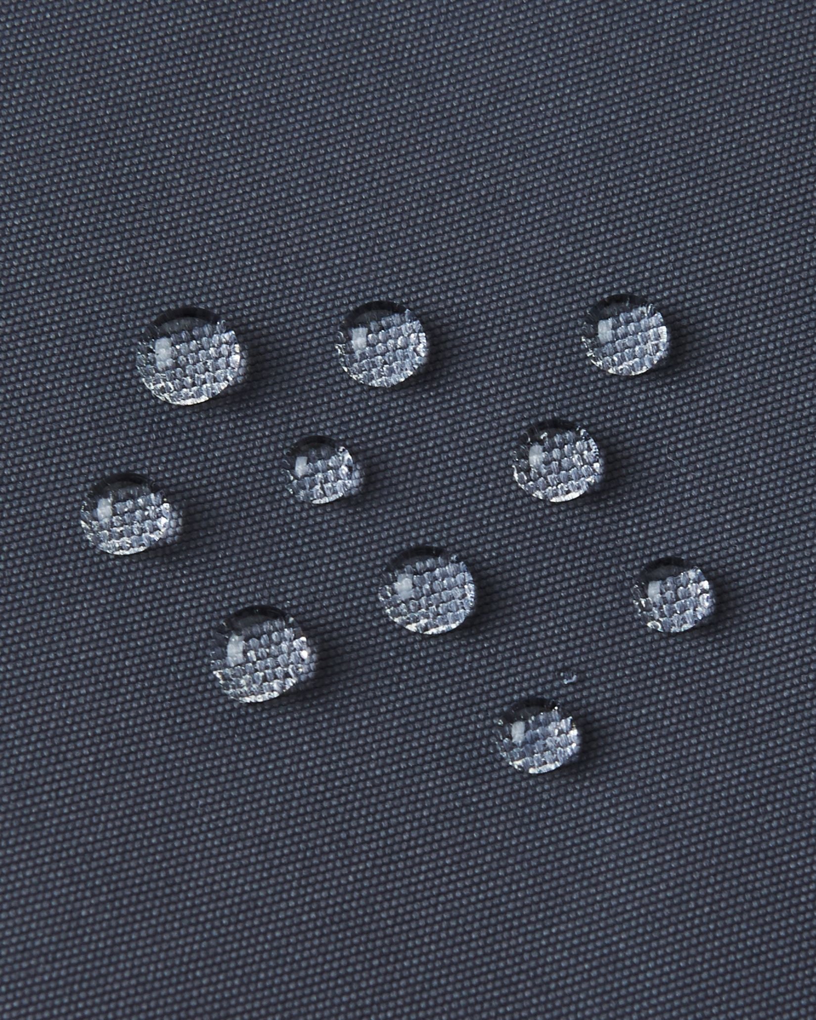 Macro close-up of water droplets tightly beading on the soft black Reimatec fabric of the Reima Reach kids' ski suit, demonstrating its extreme high-performance waterproof and weather-resistant surface capabilities.