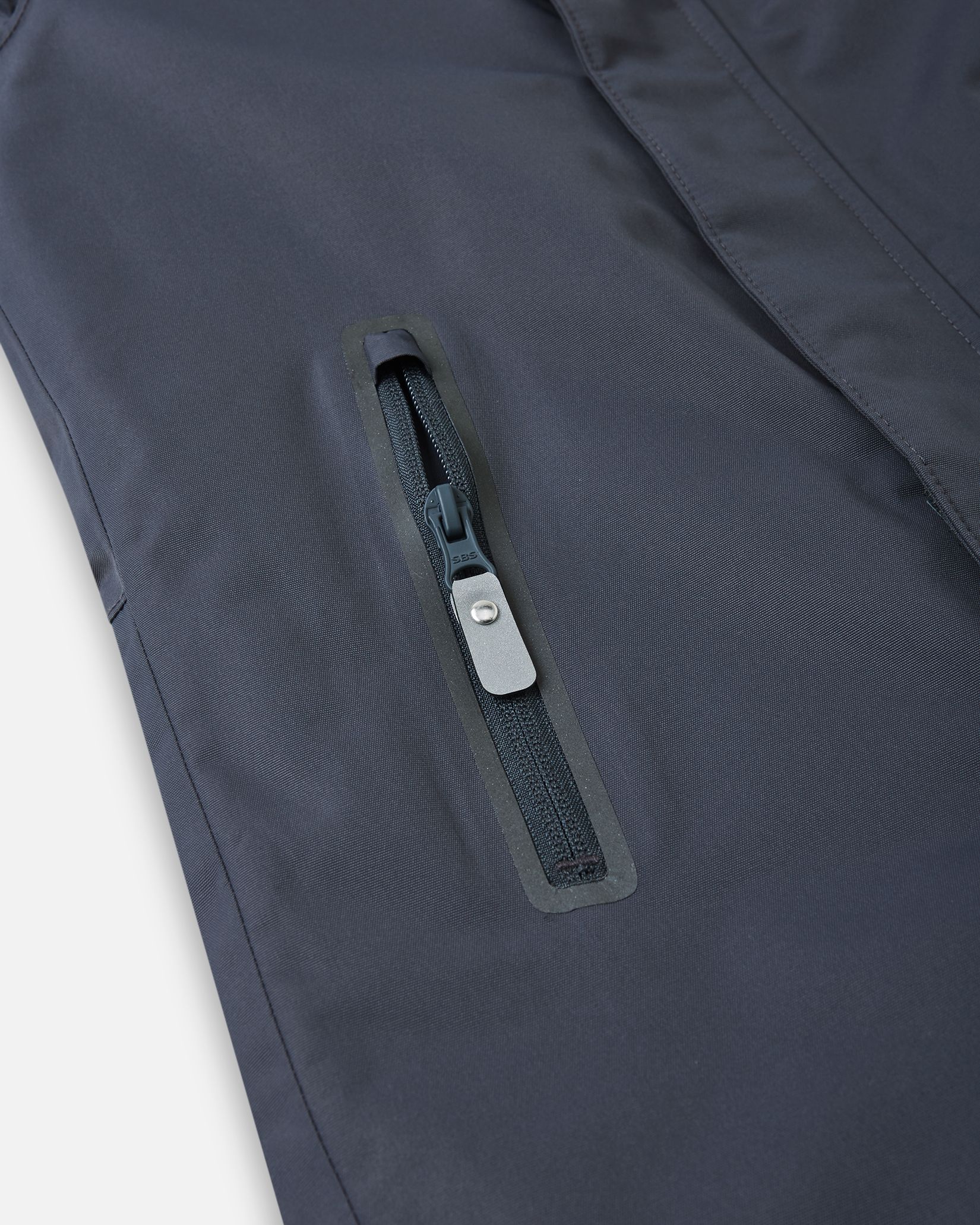 Close-up of a highly durable, water-resistant zippered pocket on the soft black Reima Reach kids' ski suit, designed with protective taping to safely store small winter essentials while keeping moisture completely out.