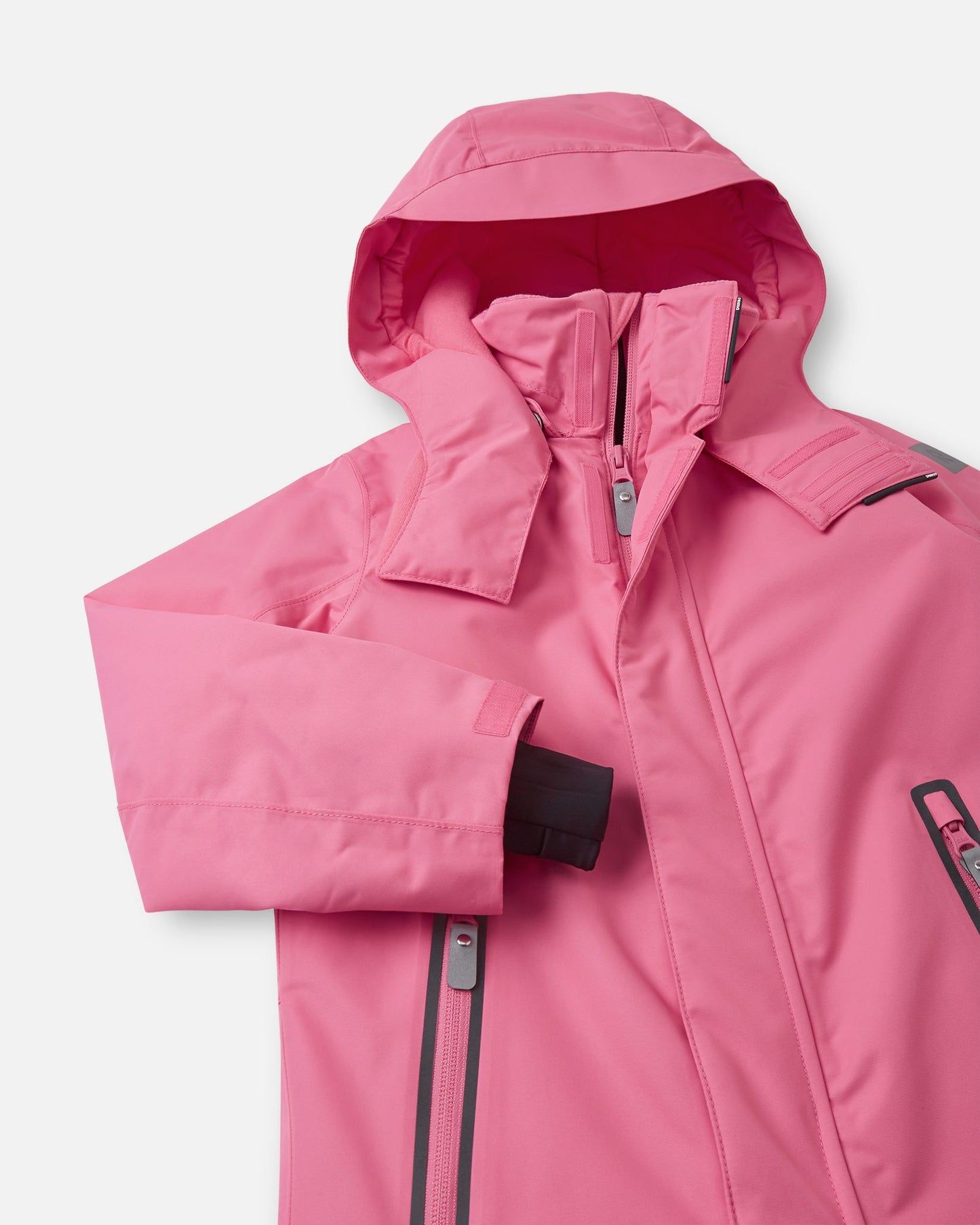 Detailed upper front view of the soft coral Reima Reach ski suit, highlighting the smooth central zipper, accessible chest pockets, and a child-safe detachable hood with a protective fleece-lined chin guard.