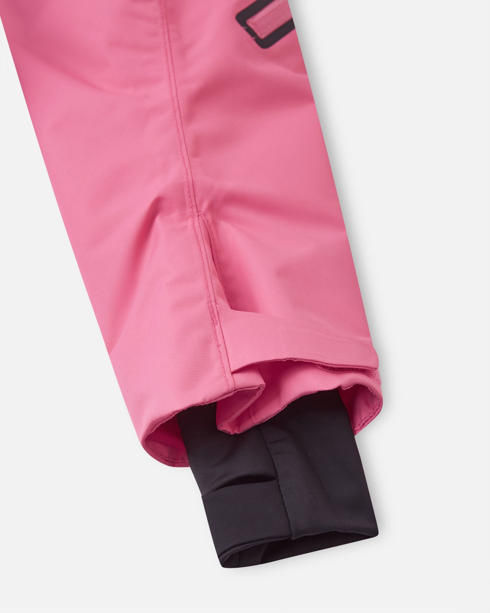 Close-up of the Reima Reach kids' ski suit sleeve in soft coral, featuring adjustable outer velcro cuffs and snug inner lycra cuffs with thumb holes to completely lock out snow and cold drafts.