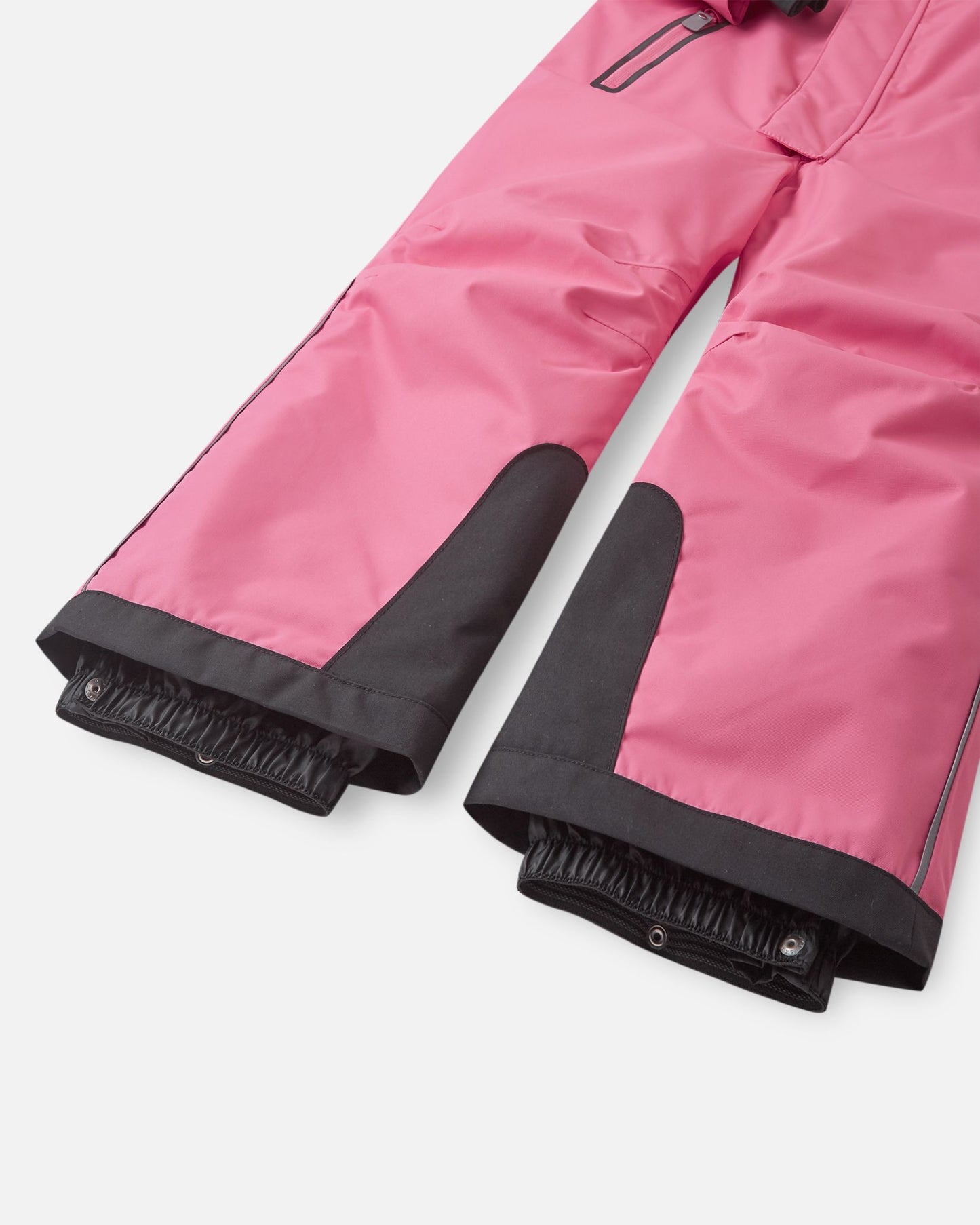 Detail shot of the lower legs on the Reima Reach kids' ski suit, showing the ultra-durable black reinforced kick patches and inner elastic snow gaiters designed to stretch tightly over ski boots.