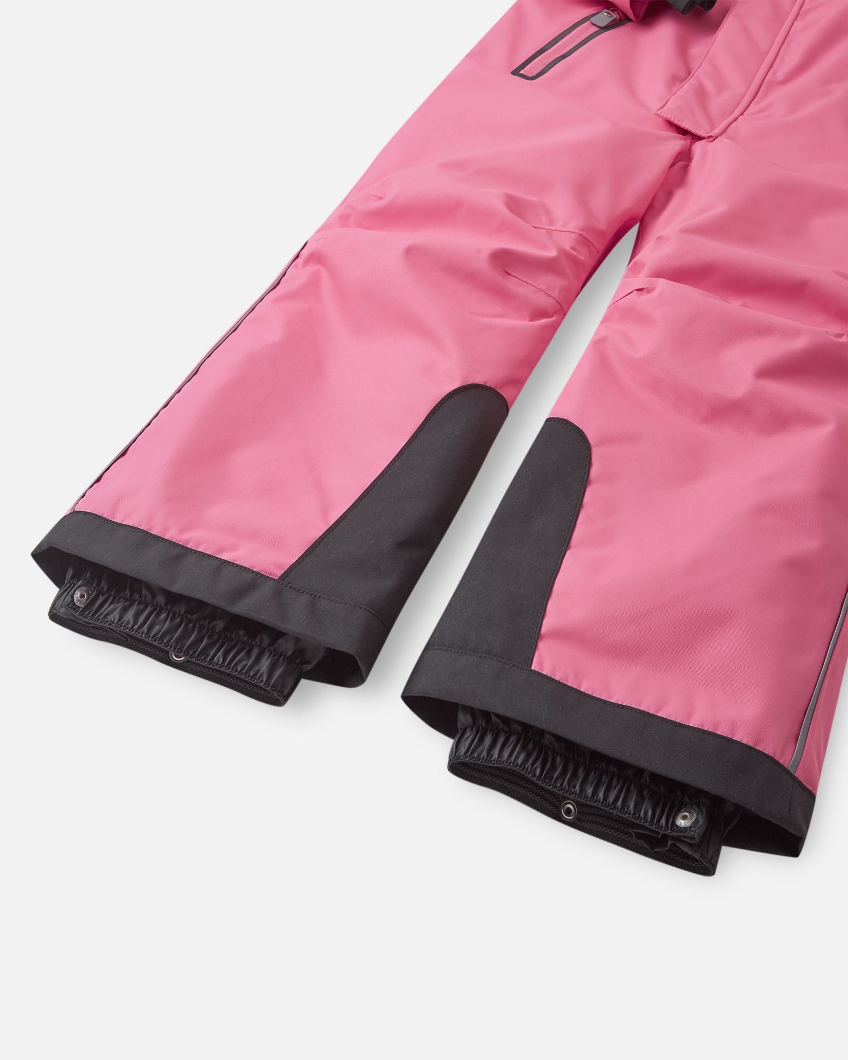 Detail shot of the lower legs on the Reima Reach kids' ski suit, showing the ultra-durable black reinforced kick patches and inner elastic snow gaiters designed to stretch tightly over ski boots.