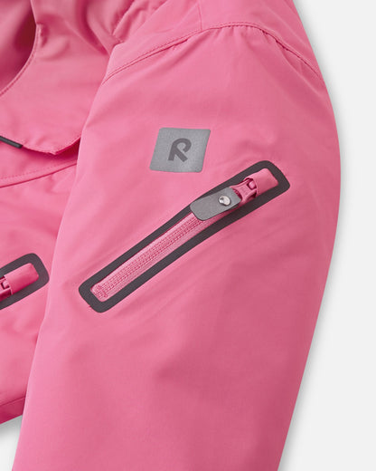 Close-up of the sleeve on the soft coral Reima Reach ski suit, featuring a secure zippered ski pass pocket on the forearm and a high-visibility reflective Reima logo patch.