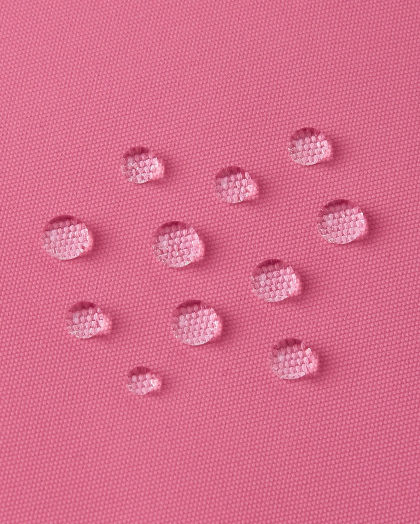Macro close-up of water droplets tightly beading on the soft coral Reimatec fabric of the Reima Reach kids' ski suit, demonstrating its high-performance waterproof and weather-resistant surface.