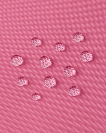 Macro close-up of water droplets tightly beading on the soft coral Reimatec fabric of the Reima Reach kids' ski suit, demonstrating its high-performance waterproof and weather-resistant surface.
