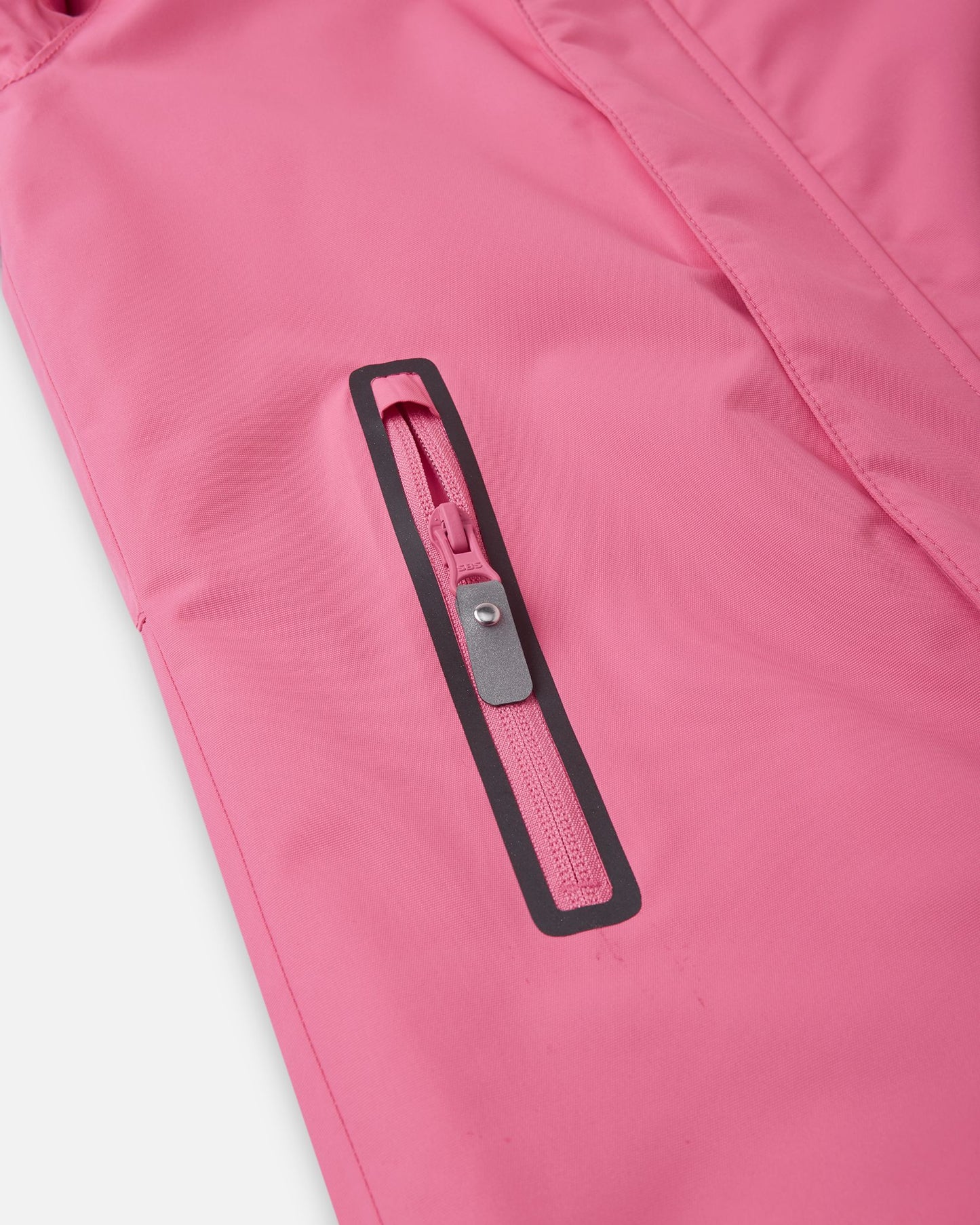 Close-up of a highly durable, water-resistant zippered chest pocket on the soft coral Reima Reach kids' ski suit, perfectly sized for safely storing a ski pass or small winter essentials on the slopes.