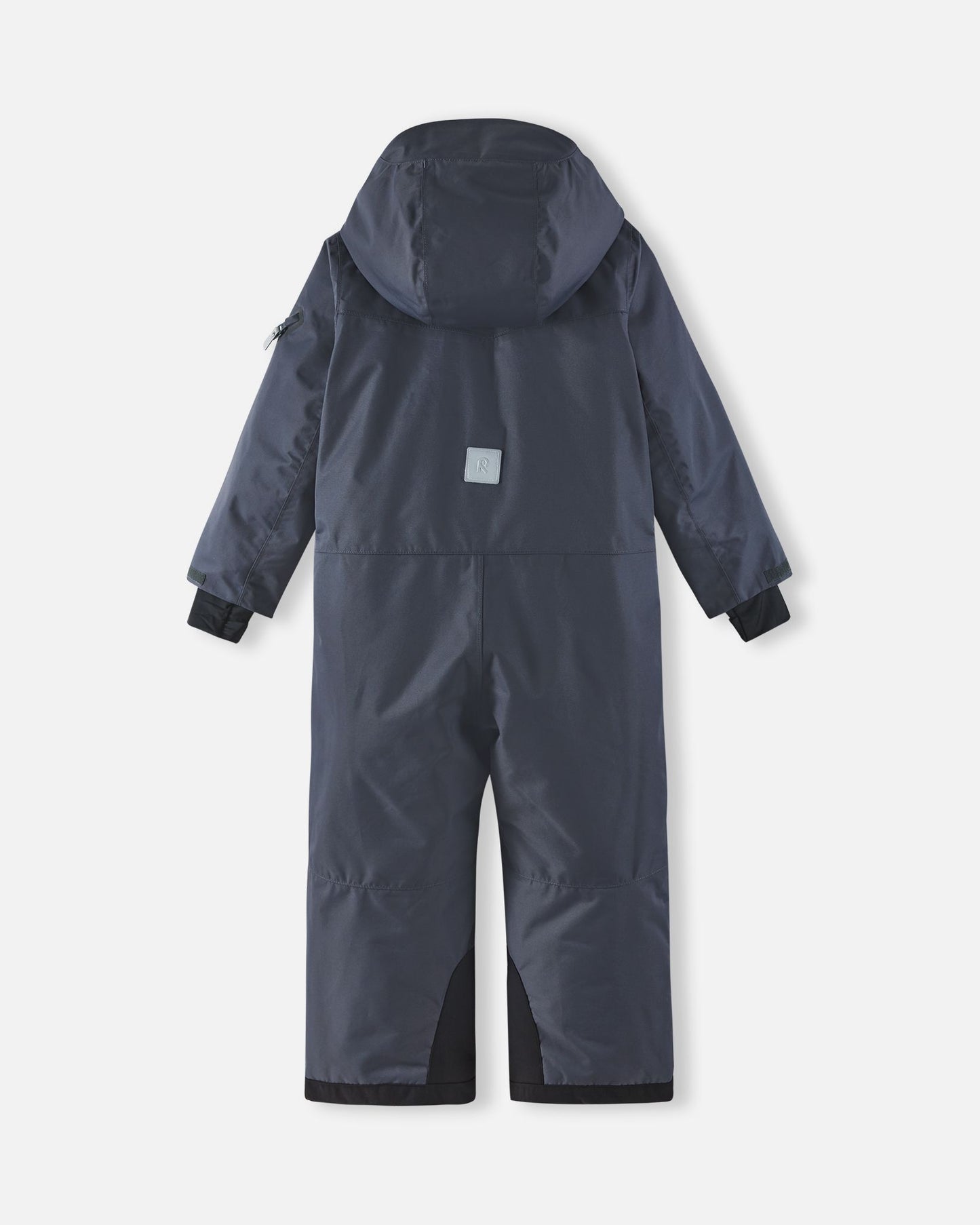 Full back view of the Reima Reach kids' ski suit in soft black, highlighting the attached winter hood, a high-visibility reflective safety patch centered on the back, and heavy-duty black reinforced seat and ankle panels.