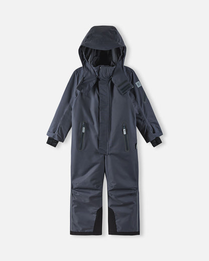 Full front view of the soft black Reima Reach kids' winter ski suit with the helmet-compatible hood pulled up, demonstrating the full-coverage weather protection and ergonomic design ideal for active winter sports.