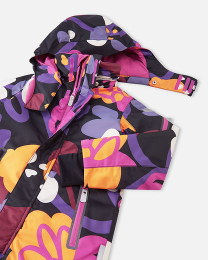 Close-up of the upper body of the Reima Reach ski suit, revealing a smooth front zipper protected by a weather-blocking wind flap, accessible chest pockets, and a child-safe detachable hood partially unfastened from the fleece-lined high collar.