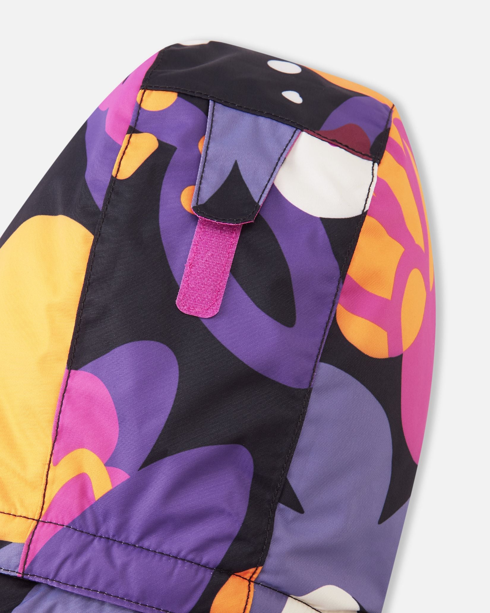 Detail view of the back of the hood on the Reima Reach kids' ski suit, showing a bright pink velcro adjustment strap that allows parents to easily customize the hood depth for a secure, safe fit over a ski helmet or winter beanie.