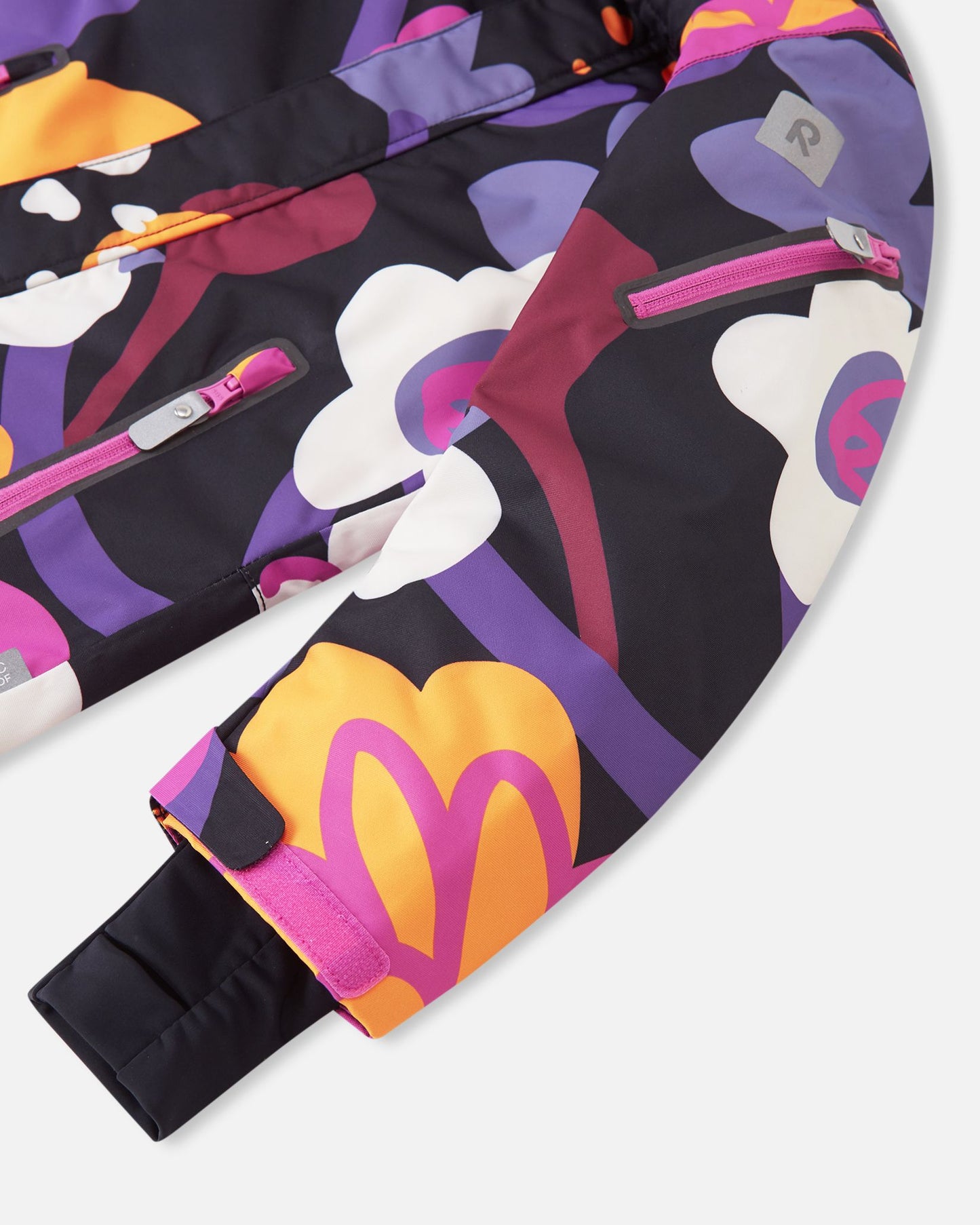 Close-up of the sleeve on the Reima Reach ski suit in the black floral print, featuring a handy zippered ski pass pocket on the lower arm, adjustable velcro outer cuffs, and snug stretch inner cuffs to lock out snow and cold drafts.
