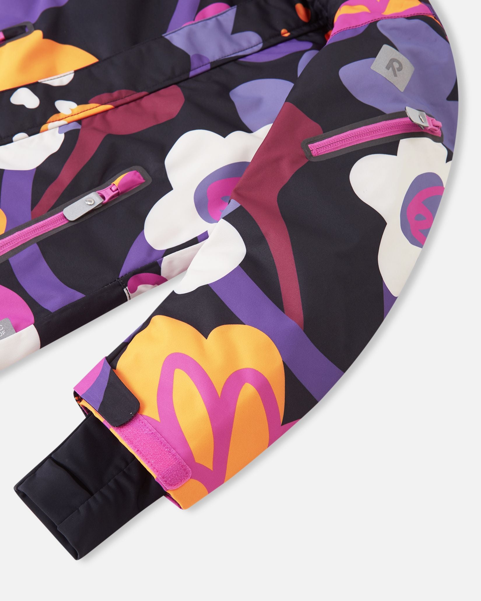Close-up of the sleeve on the Reima Reach ski suit in the black floral print, featuring a handy zippered ski pass pocket on the lower arm, adjustable velcro outer cuffs, and snug stretch inner cuffs to lock out snow and cold drafts.
