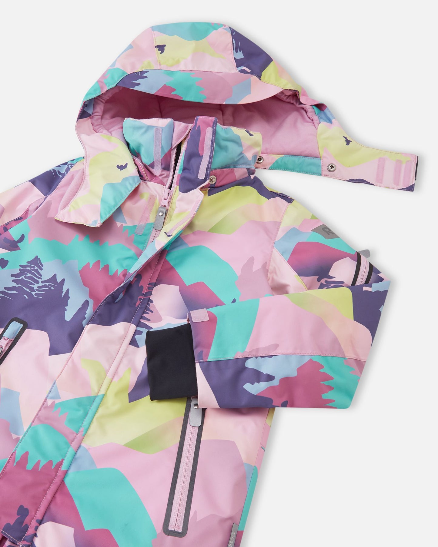 Close-up of the upper half of the Reima Reach ski suit, highlighting the smooth front zipper covered by a protective wind flap, secure zippered chest pockets, and the safe, detachable hood partially unsnapped from the high collar.