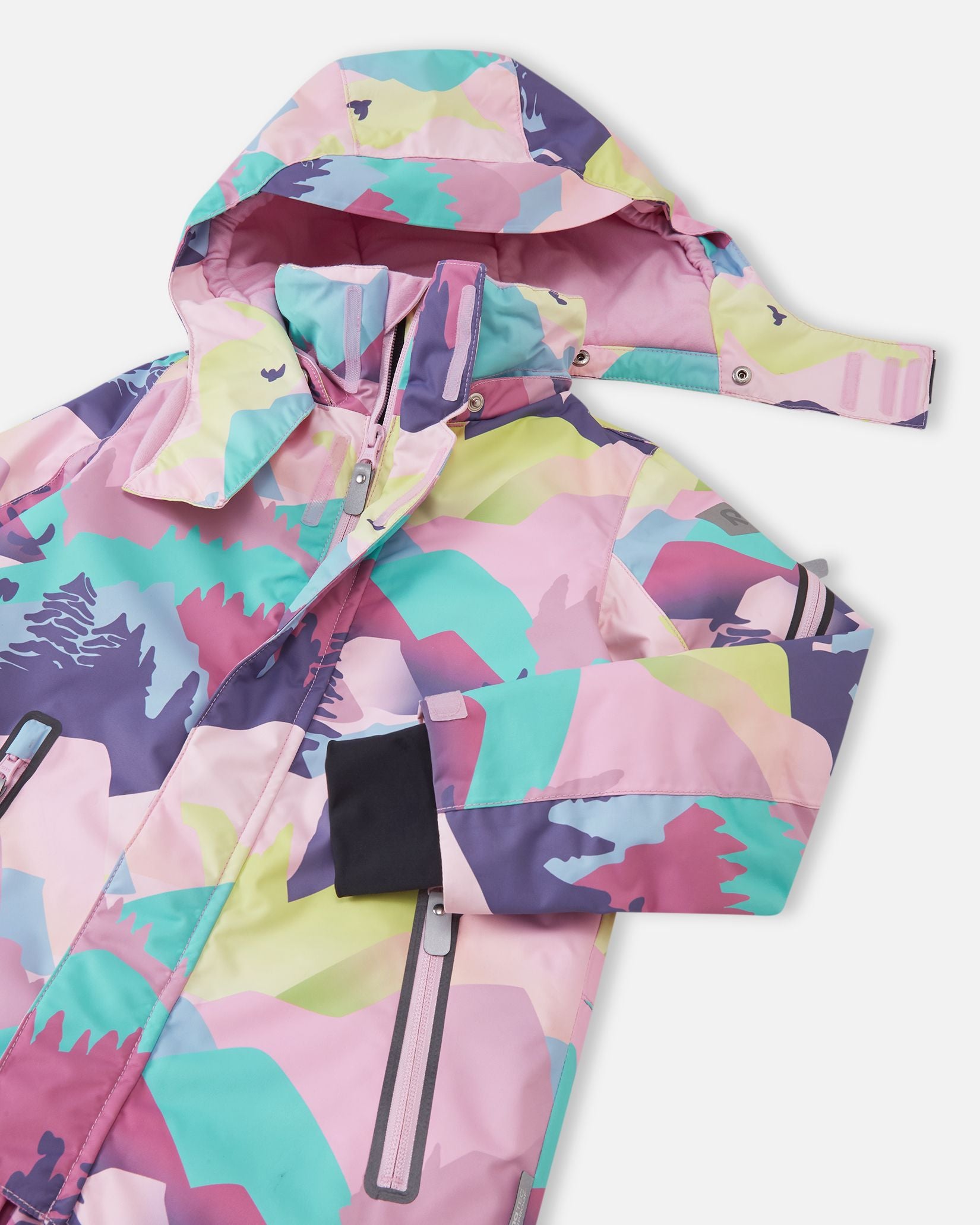 Close-up of the upper half of the Reima Reach ski suit, highlighting the smooth front zipper covered by a protective wind flap, secure zippered chest pockets, and the safe, detachable hood partially unsnapped from the high collar.