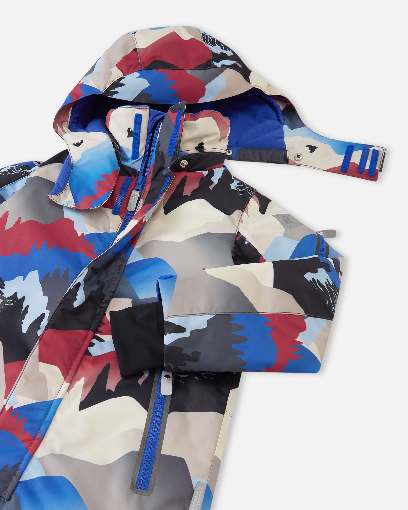 Close-up of the upper half of the Reima Reach ski suit, highlighting the smooth front zipper shielded by a secure wind flap, accessible zippered chest pockets, and the child-safe detachable hood partially unsnapped from the high stand collar.