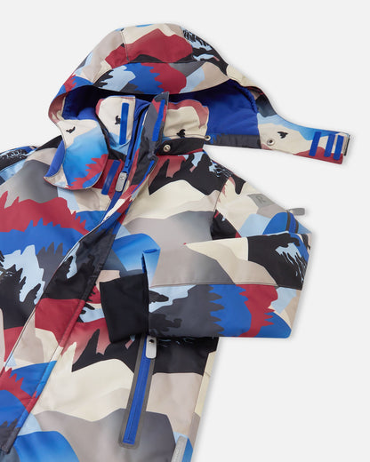 Close-up of the upper half of the Reima Reach ski suit, highlighting the smooth front zipper shielded by a secure wind flap, accessible zippered chest pockets, and the child-safe detachable hood partially unsnapped from the high stand collar.
