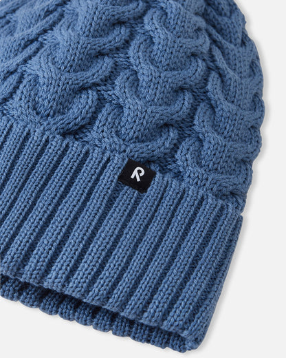 Close-up macro detail of the ribbed fold-up hem on the blue ocean Reima Routii kids' beanie, featuring the woven black Reima reflective label and the premium merino wool-mix yarn texture.