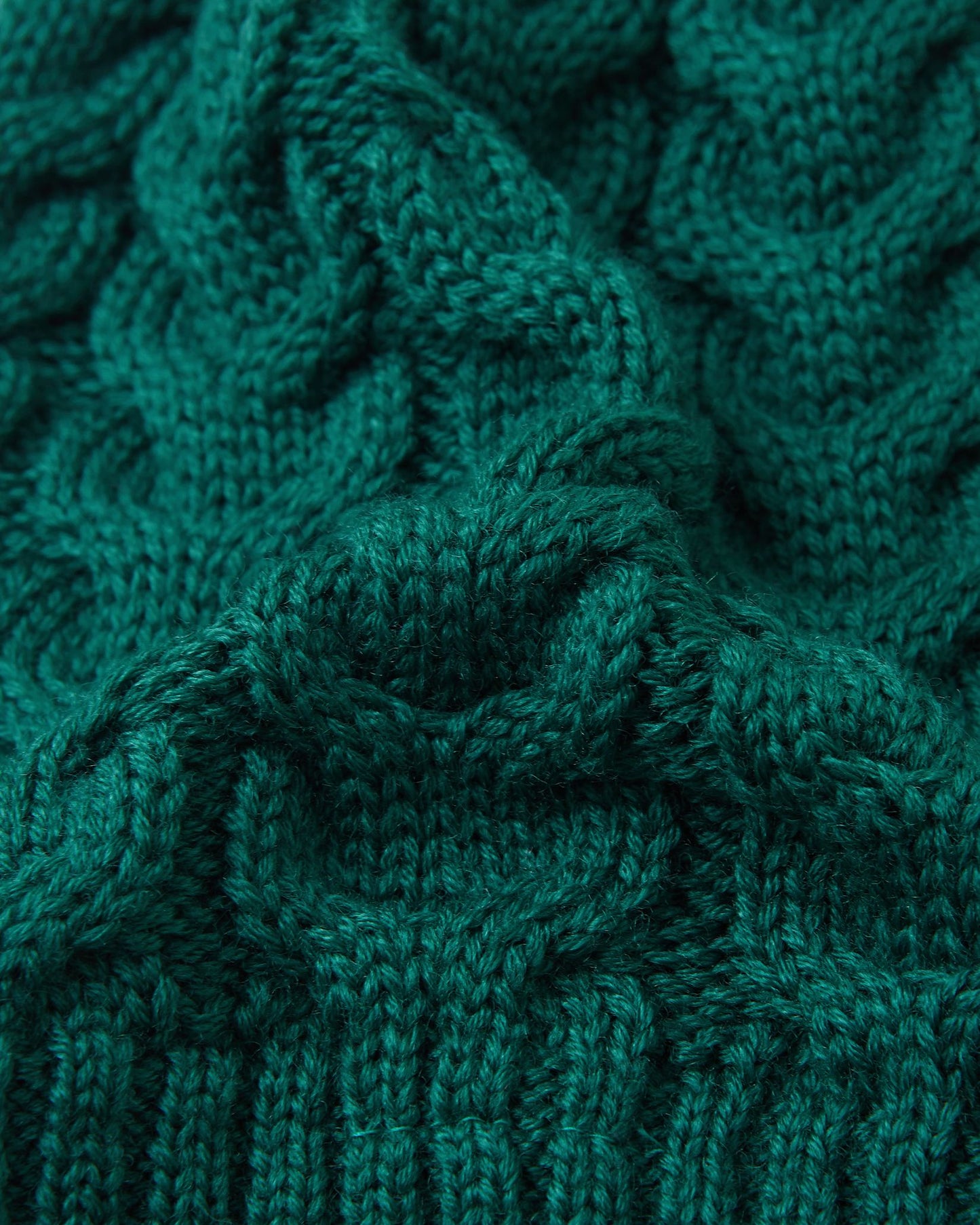 Macro close-up of the thick, intricate cable knit structure on the deeper green Reima Routii kids' winter hat, demonstrating the high-quality texture and flexibility of the warm merino wool-blend yarn.