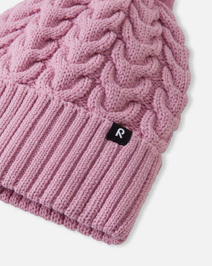 Close-up macro detail of the ribbed fold-up hem and thick cable knit structure on the grey pink Reima Routii kids' winter hat, featuring the woven black Reima reflective label and the premium merino wool-mix yarn.