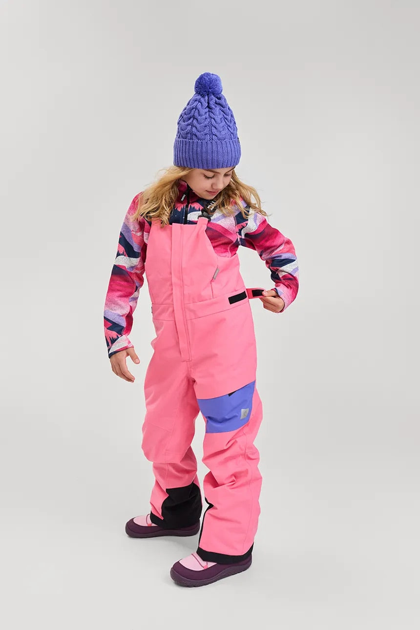 Young girl wearing the breezy violet Reima Routii knitted merino wool beanie and pink ski overalls, adjusting her gear.