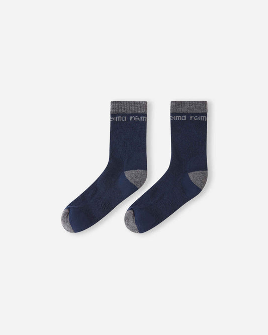 Flat lay view of a pair of Reima Saapas kids' wool blend socks in classic navy blue, showcasing the warm crew length design with contrasting dark grey reinforced heels and toes.