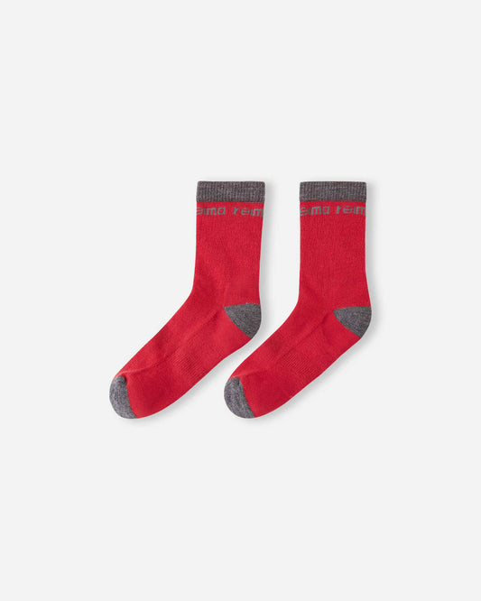Flat lay view of the Reima Saapas kids' wool blend winter socks in Reima red, featuring a comfortable crew length, dark grey reinforced wear zones, and a soft knit construction for cold weather.