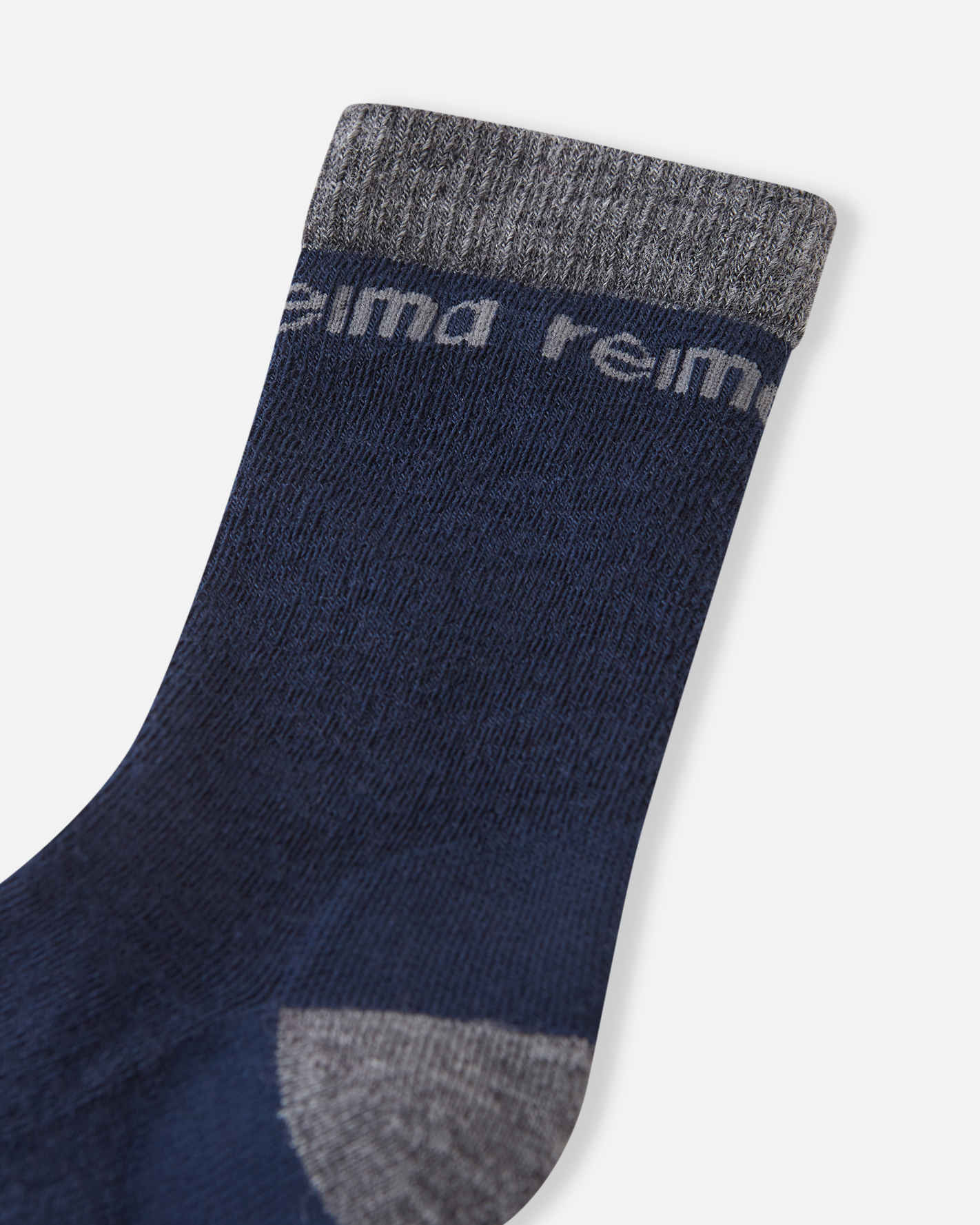 Close-up detail of the upper section on the navy blue Reima Saapas kids' winter socks, focusing on the dark grey ribbed ankle cuff and the tonal grey woven Reima logo.