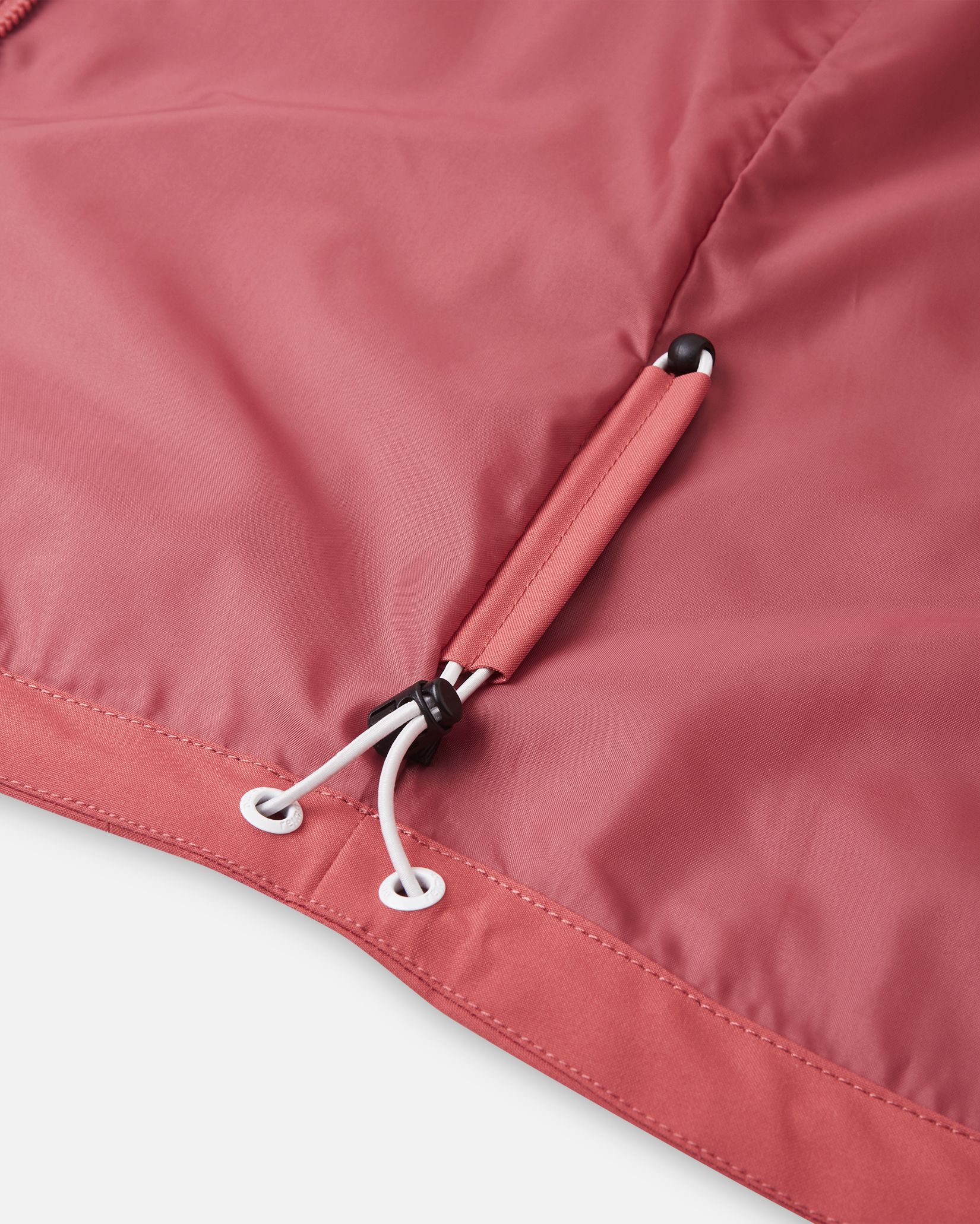 Close-up of the inner hem on the Reima Saarela kids' red clay shell jacket, detailing the adjustable bungee cord and toggle system designed to seal out wind and retain body heat.
