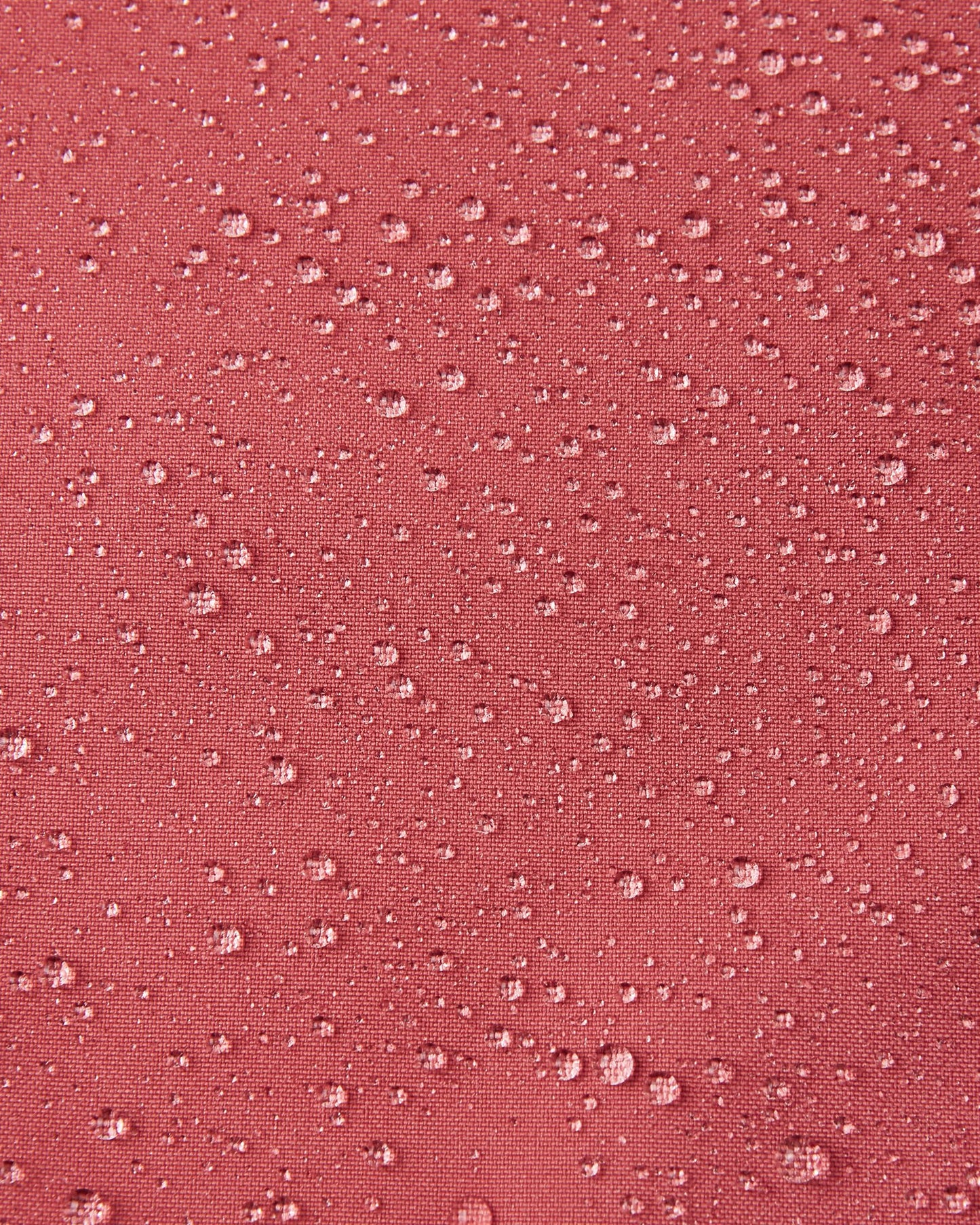 Macro close-up of water droplets beading up and rolling off the surface of the Reima Saarela kids' red clay shell jacket, demonstrating the highly waterproof and dirt-repellent Reimatec material.
