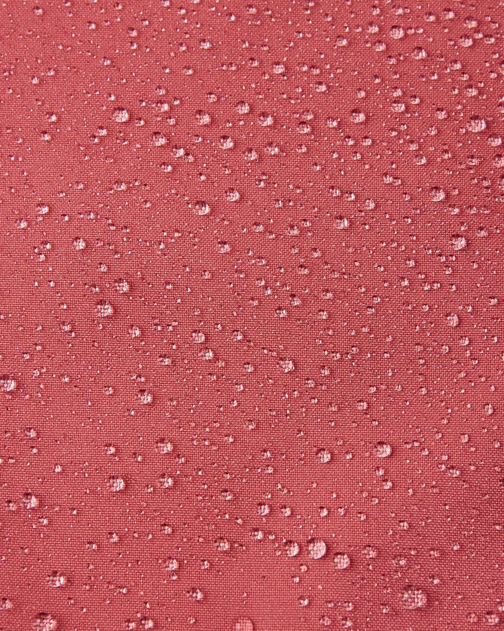 Macro close-up of water droplets beading up and rolling off the surface of the Reima Saarela kids' red clay shell jacket, demonstrating the highly waterproof and dirt-repellent Reimatec material.