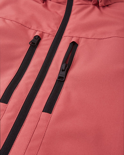 Close-up detail of the Reima Saarela kids' red clay shell jacket, highlighting the two secure zippered chest pockets with durable black hardware set against the waterproof fabric.