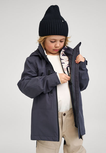 A young child adjusting the zipper of the soft black Reima Saarela waterproof jacket, revealing a warm mid-layer zipped comfortably inside.